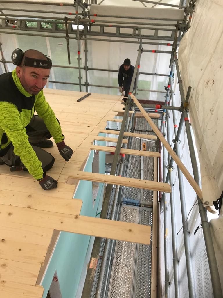 Snickare som lägger skivor på ett bjälklag intill ställningen, med en kollega längre bort.